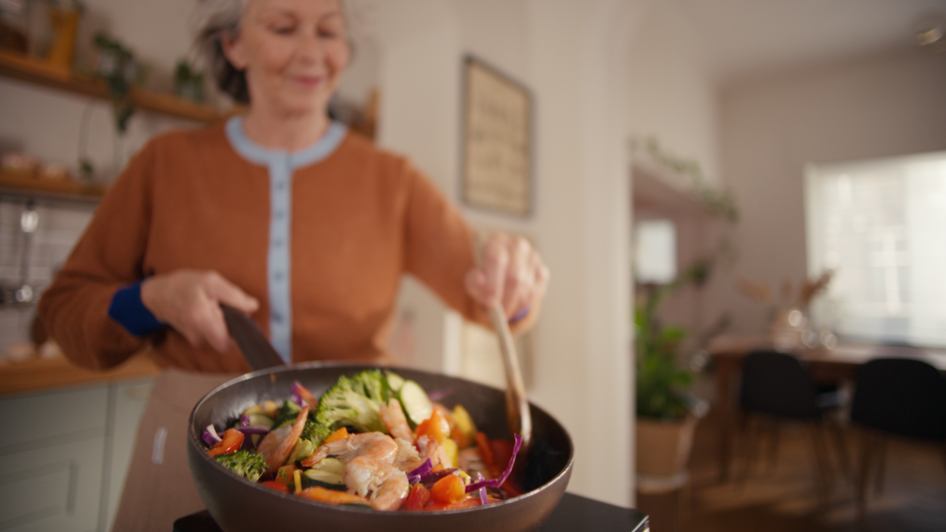 En leende kvinna som vänder en räkwok i stekpannan och skapar matos i köket