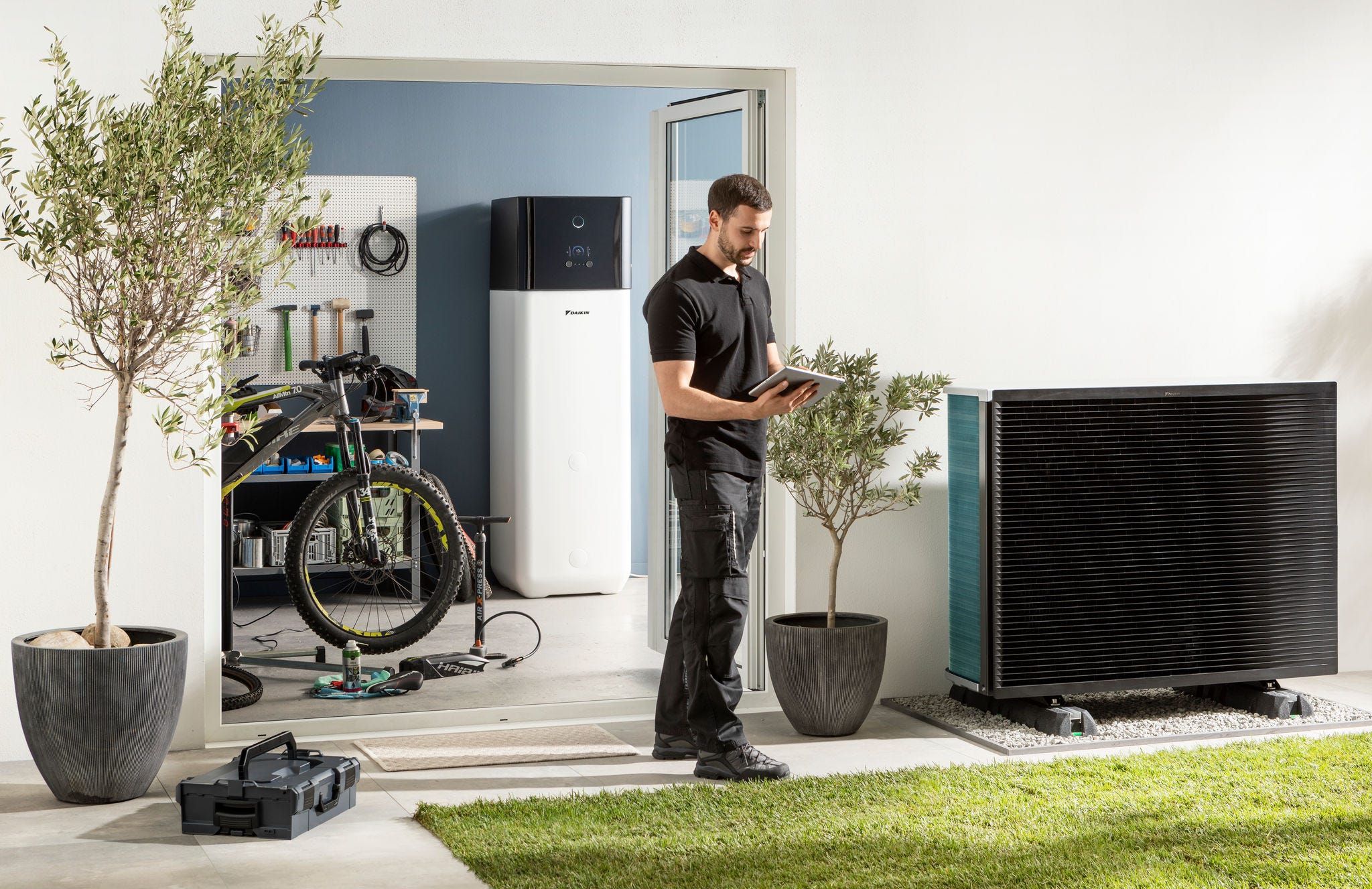 Installatör som kontrollerar utomhusenheten till en luft/vattenvärmepump samt varmvattentanken