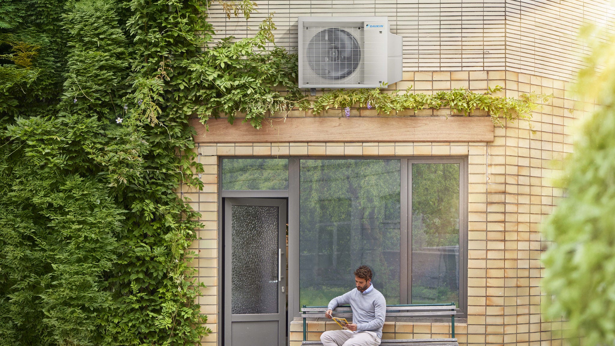 Man som sitter och läser på en bänk utanför sitt hus under en Daikin luftvärmepump.