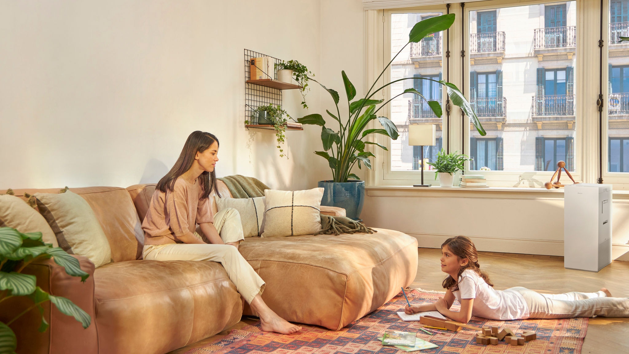 Mor och dotter kopplar av och njuter av ren luft i vardagsrummet, medan dottern ritar och mamman sitter i soffan