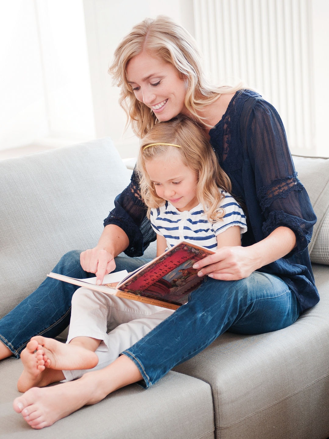 En mamma sitter på soffan med sin lilla dotter i knät, och de tittar i en bok