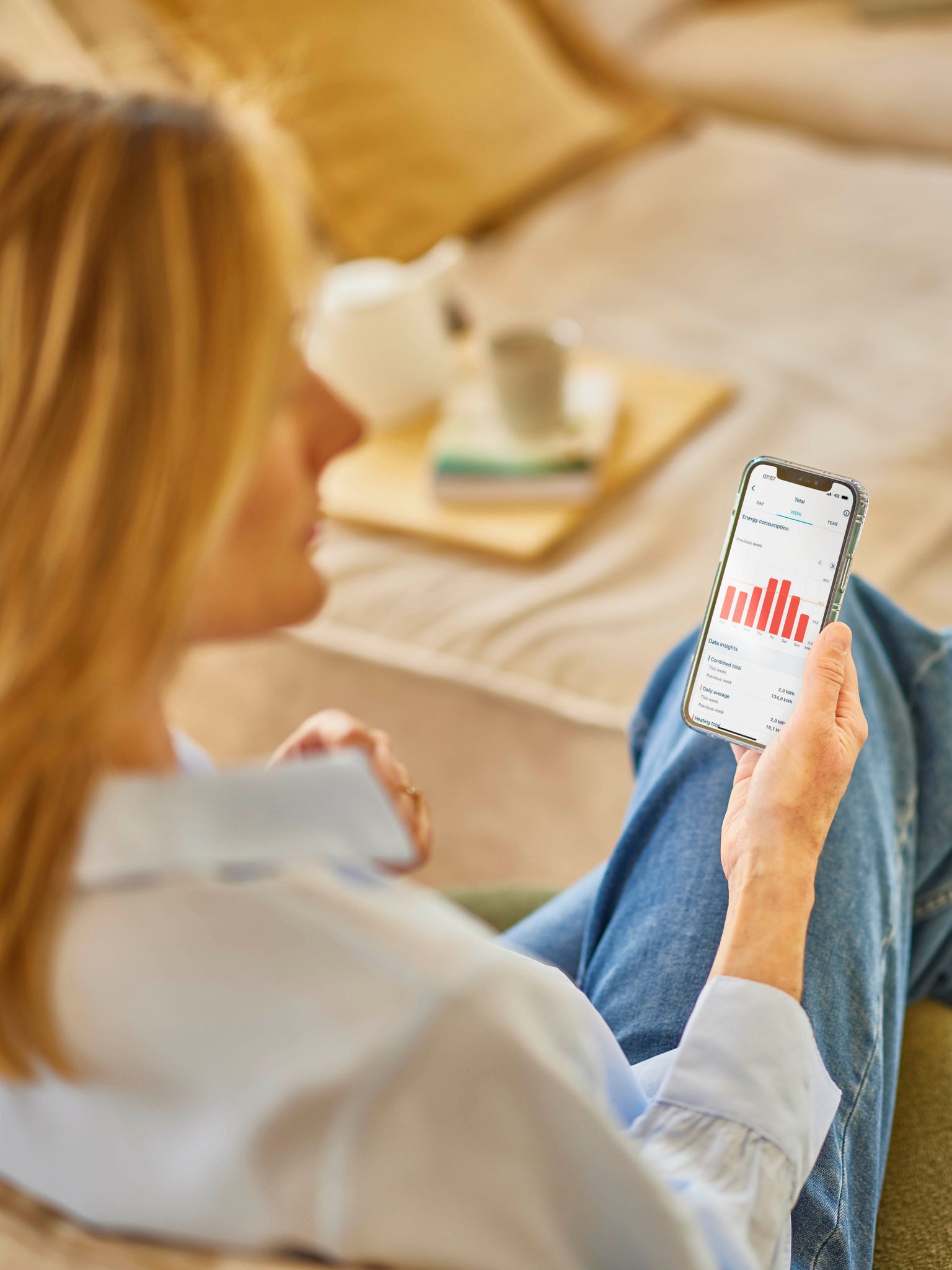 En blond kvinna som tittar på sin energiförbrukning i en app på sin mobiltelefon