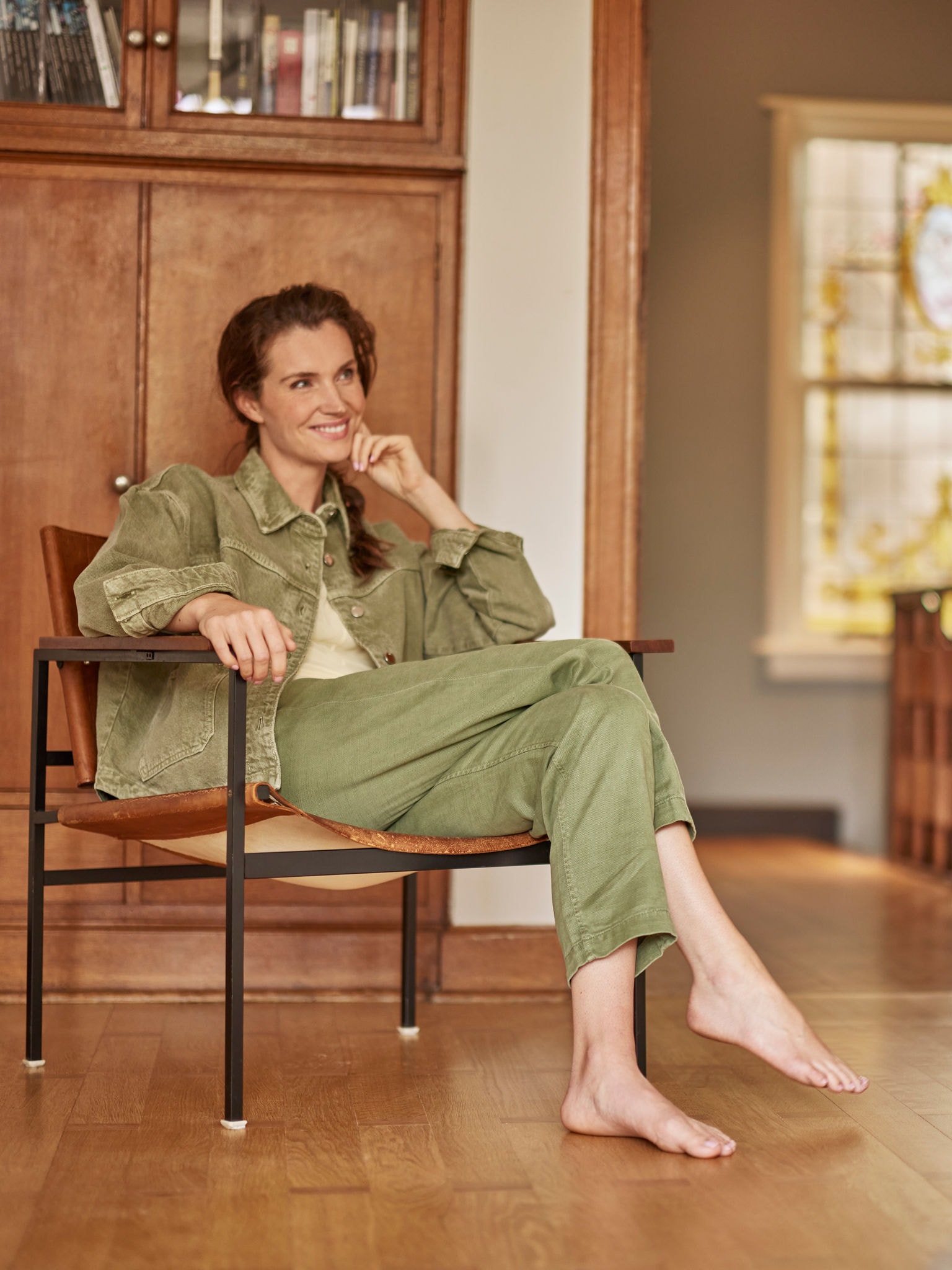 Kvinna som sitter barfota i sin fåtölj, ler och blickar framåt