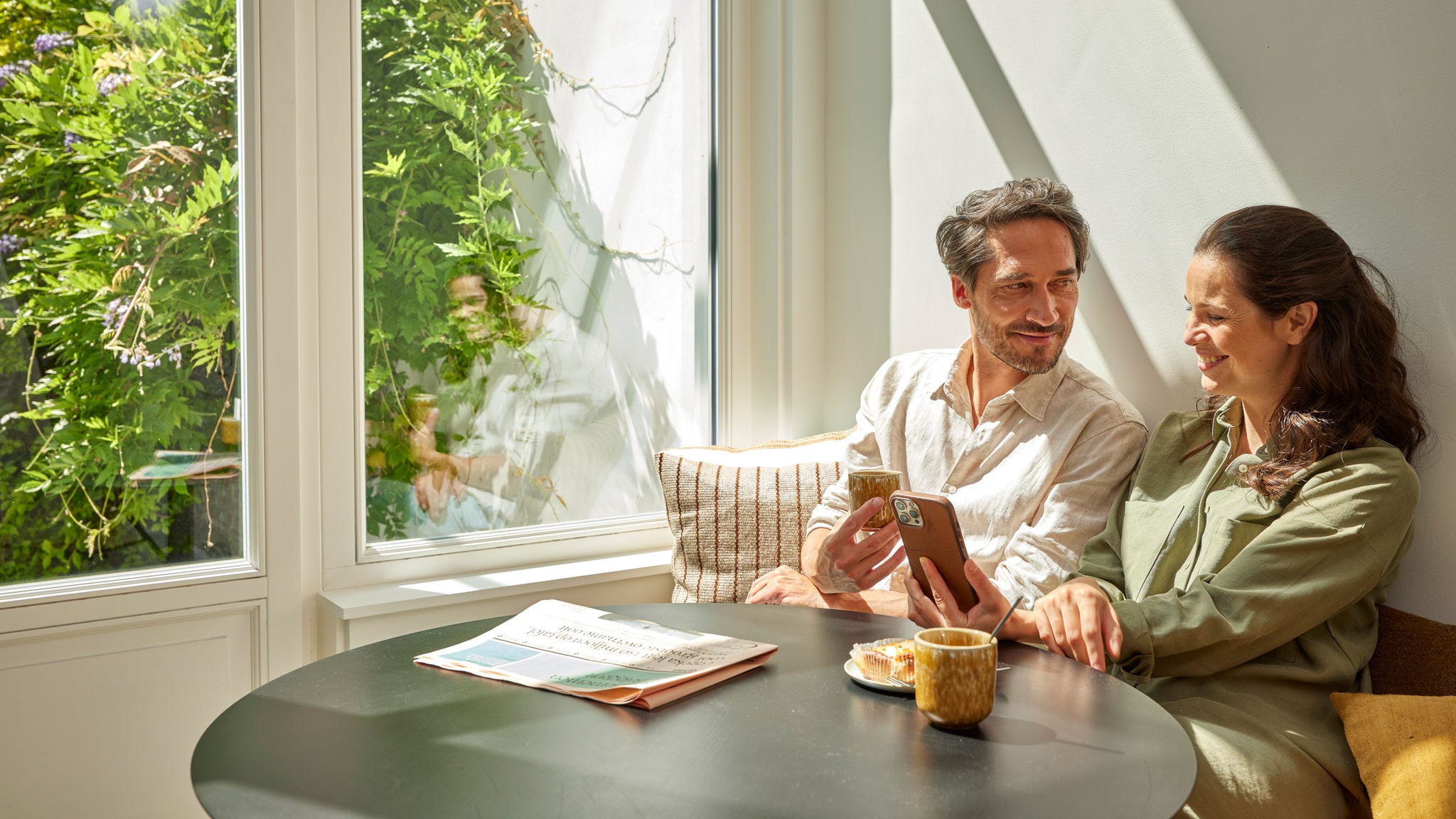 Ett par som njuter av kaffe och tittar på energibesparingar på deras telefon och visar upp kostnadsminskningar genom att använda en värmepump