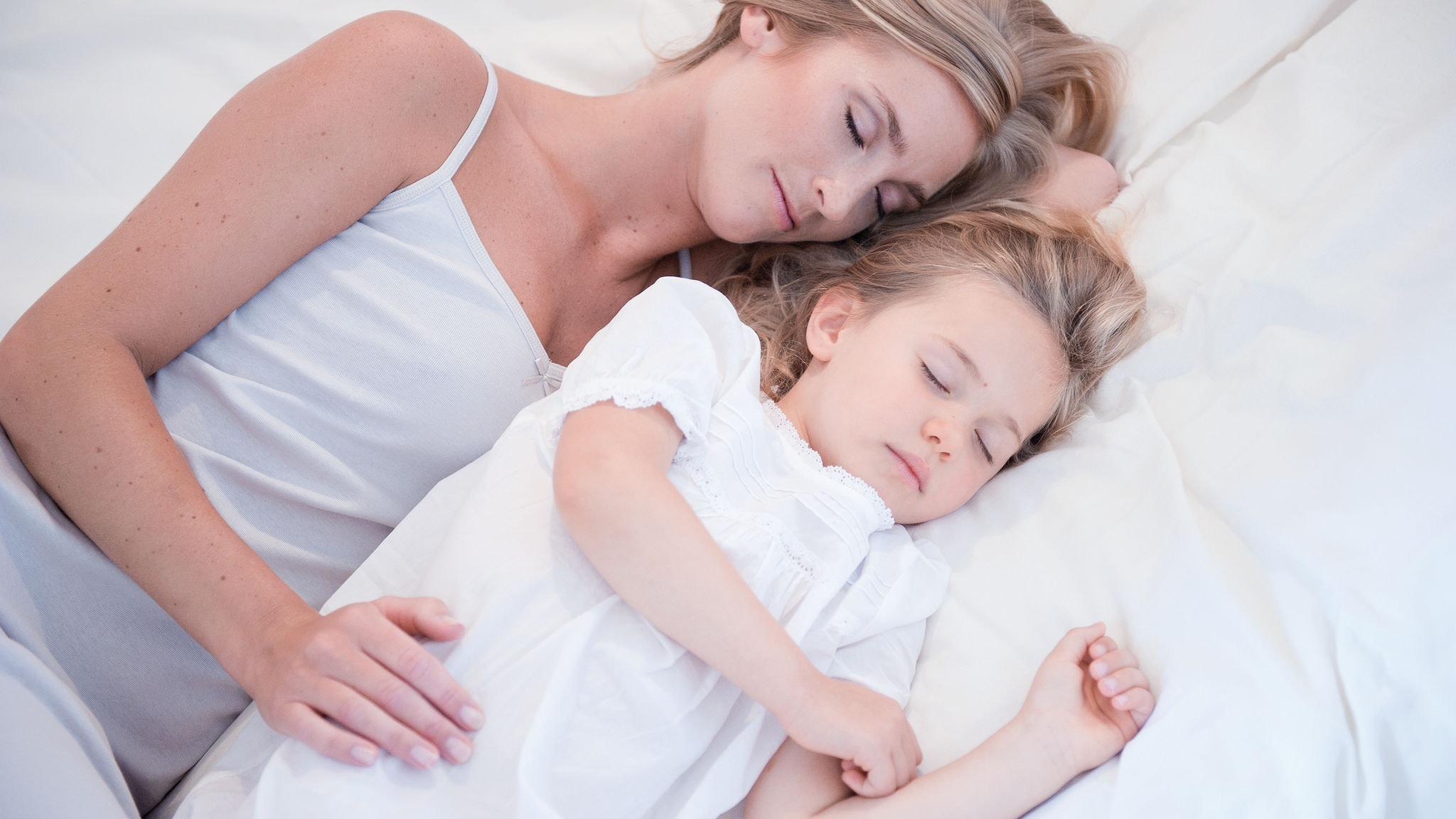 En mamma och hennes lilla dotter som sover bredvid varandra i en vit säng i ren luft