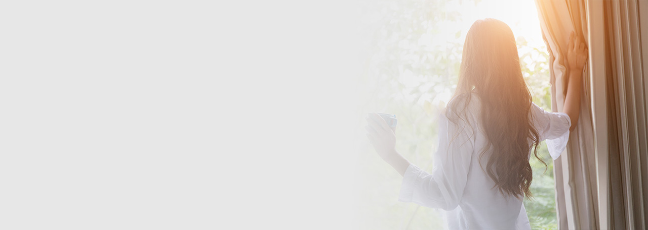 Kvinna som tittar ut samtidigt som hon håller i gardinen.